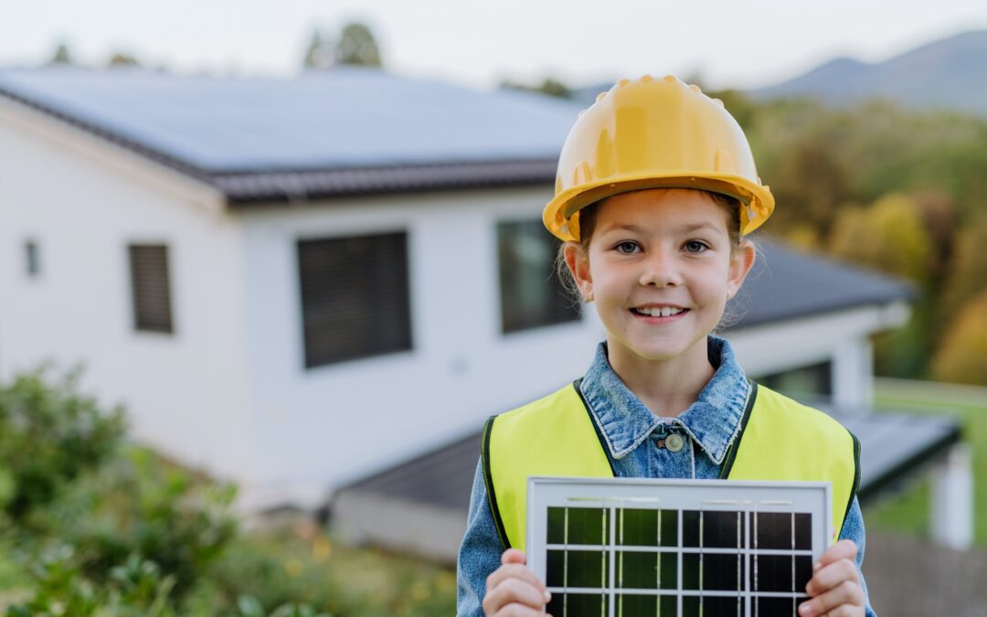 Little girl with protective helmet and reflective vest holding photovoltaics solar panel